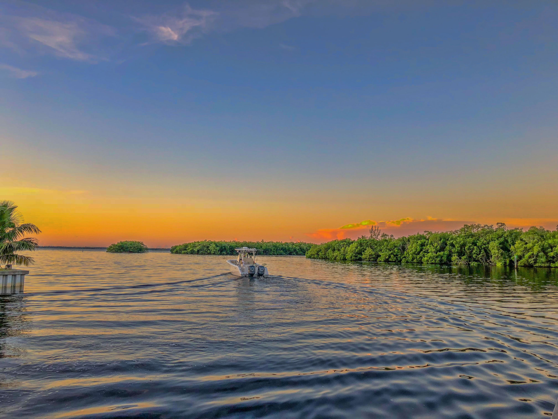 Westwind Waterman charter boat cruising toward mangrove islands under a colorful Gulf Coast sunset